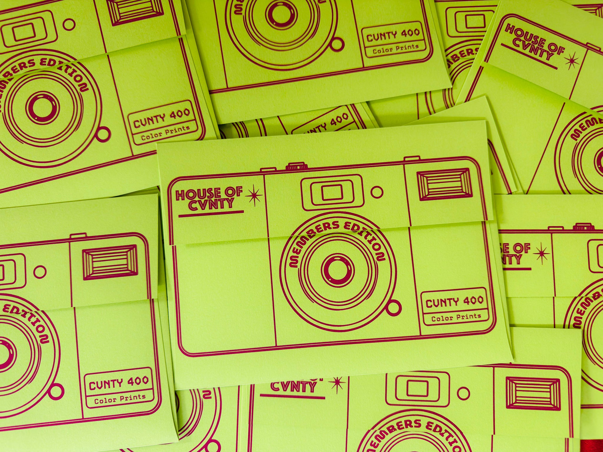 Bright lime green instant camera-themed envelopes with dark red printed graphics and text reading 'HOUSE OF CVNTY MEMBERS EDITION' and 'CUNTY 400 Color Prints', arranged in a flat-lay pattern.